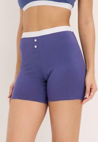 Shorts en coton violet au design ajusté, avec une taille élastique blanche et deux boutons décoratifs à l'avant. Texture lisse et sans motifs.