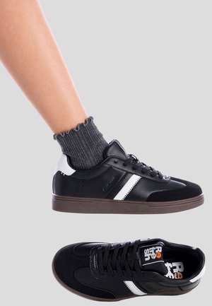 Zapatilla deportiva casual en blanco y negro usada con calcetines hasta el tobillo de color gris oscuro con volantes, con un segundo zapato idéntico colocado debajo.