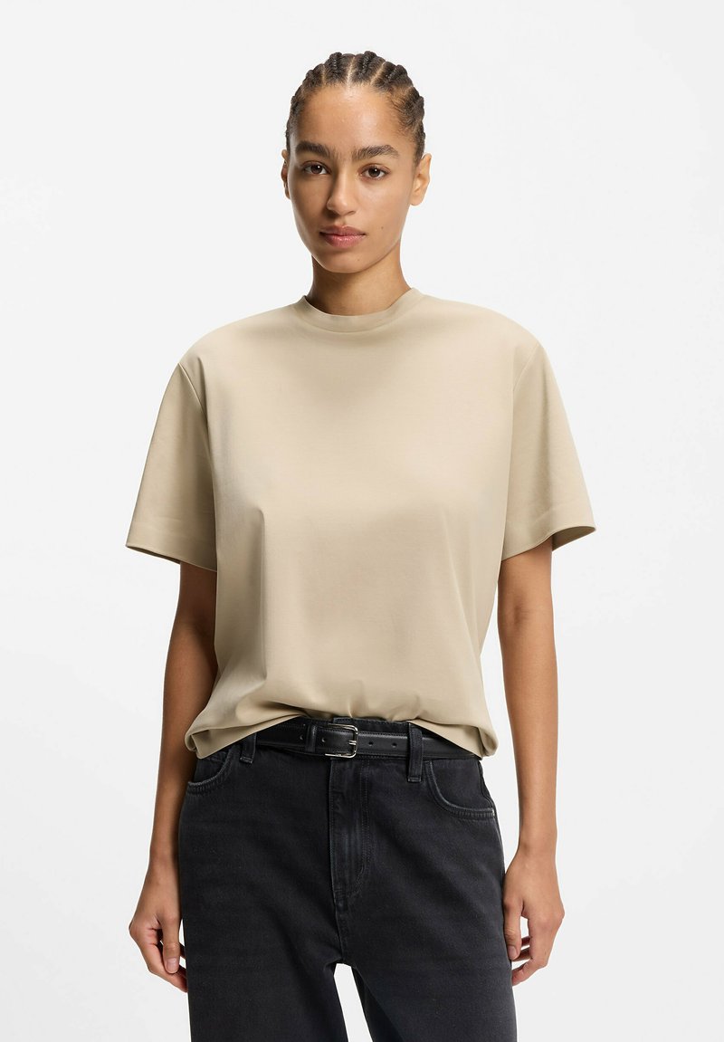 Beige short-sleeve t-shirt with a round neckline, made of smooth fabric, paired with black high-waisted jeans and a black belt.