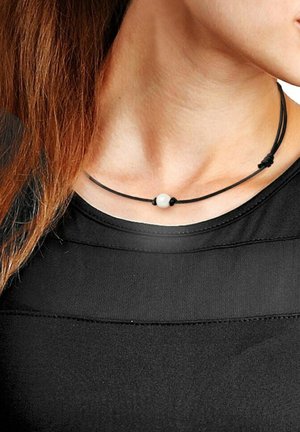 Collier en cordon noir avec une perle blanche centrale, design ajustable, porté autour du cou, complète un haut noir. Style simple et minimaliste.