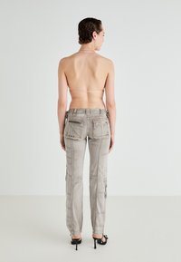 Grey cargo pants with a slim fit, multiple pockets, and zipper details. Fabric texture appears robust. Worn with black high-heeled shoes.