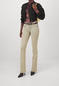 Chaqueta bomber negra, blusa de manga larga colorida, jeans rectos beige, tacones negros de punta y un bolso amarillo.