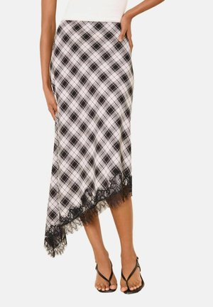 Naine kannab must-valget ruudulist asümmeetrist midi-seelikut musta pitsi äärisega, millele on lisatud mustad avatud varbaga kontsad ja valge top.