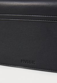 Sac en faux cuir noir avec surface texturée, ornée du logo "HVISK" en relief et d'un détail de couture contrastant le long des bords.