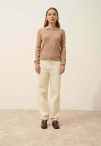 Brauner gerippter Strickpullover mit einem halben Reißverschlusskragen, kombiniert mit lockeren cremefarbenen Hosen und dunkelbraunen Absatzschuhen. Schlichtes, modernes Aussehen.