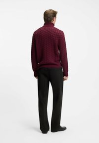 Maglione a collo alto in maglia cable-knit color bordeaux con orlo a coste e texture, abbinato a pantaloni neri su misura e scarpe nere.