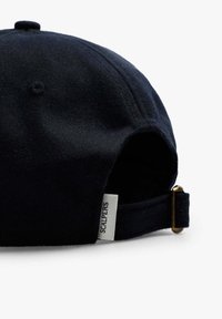 Marinepet met een gestructureerde stof, een verstelbare band en een klein merkembleem aan de zijkant. Kenmerkt zich door een afgeronde kroon en een knoopdetail.