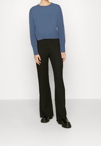 Blå texturerad tröja med långa ärmar, parat med svarta utsvängda byxor med ett veckat mönster och svarta platåskor.