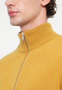 Mustár sárga cipzáras pulóver, magas bordás gallérral, sima, puha textúrával és ezüst cipzár részlettel.