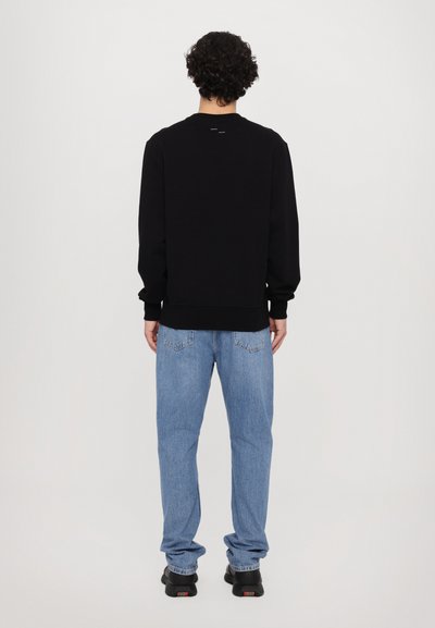 Sweatshirt noir avec un ourlet et des poignets côtelés, associé à un jean en denim bleu clair. Les baskets présentent un détail multicolore sur la semelle.