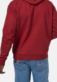 Felpa borgogna con una texture liscia, tasca a marsupio e cappuccio con cordino. Abbinata a jeans di denim blu chiaro con toppe con logo.