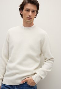 Roomkleurige gebreide trui met een gestructureerd patroon, ronde hals en geribbelde manchetten. Gedragen over blauwe spijkerbroek met een ontspannen pasvorm.