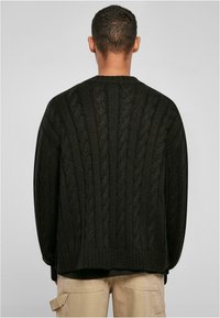 Svart kabelstrikket oversized genser med ribbestrikket hals og mansjetter, med et teksturert, vevd mønster på baksiden.