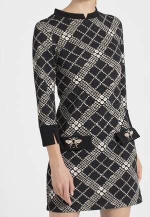 Robe à carreaux noir et blanc avec manches trois-quarts, présentant deux nœuds avec détails brodés d'abeilles près des hanches.