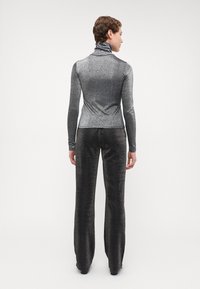 Haut en col roulé gris métallique associé à un pantalon large assorti. Les deux sont fabriqués dans un tissu texturé et scintillant avec une coupe ajustée.