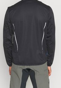 Schwarze Jacke mit einer glatten Textur, ausgestattet mit weißen Seitenakzenten und einem rundem Kragen. Der Rücken ist leicht länger mit einem geraden Saum.