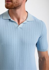 Gaiši zils ribots īsām piedurknēm polo krekls ar V-veida kakla izgriezumu, kas piedāvā teksturētu adījumu un vienkrāsainu adījuma apdari kaklam un piedurknēm.