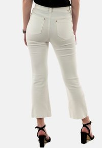 Jeans flare blancos con cintura alta, cinco bolsillos y detalles en dorado; textura suave y dobladillo sin terminar en la parte inferior.