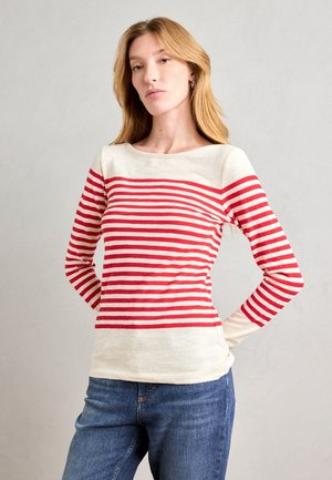 Chemise à rayures rouges et crème à manches longues, avec un col bateau et une coupe ajustée, assortie à un jean en denim bleu.