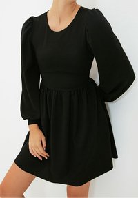 Czarna sukienka z okrągłym dekoltem, bufiastymi długimi rękawami i marszczoną talią, z rozkloszowanym dołem i gładką teksturą.