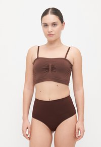 Brūns divdaļīgs bikini komplekts, kurā ietilpst croptops ar priekšējo rušēšanu un regulējamām siksnām, kopā ar augstām, saskaņotām biksēm.