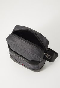 Gray fabric crossbody bag with black accents, zip closure, and adjustable strap. Features front pocket and small logo detail.