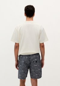 Cămașă scurtă, din crem deschis, cu mâneci scurte, asortată cu pantaloni scurți gri închis, având un model floral alb și buzunare aplicate pe spate.