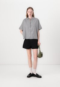 Raidallinen lyhythihainen paita, jossa on nappi edessä, yhdistetty mustiin shortseihin. Asusteina vihreä käsilaukku ja mustat loafersit valkoisilla sukilla.