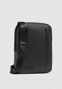 Borsa a tracolla nera in pelle strutturata. Presenta una chiusura con zip, tracolla regolabile e design minimalista con dettaglio logo.
