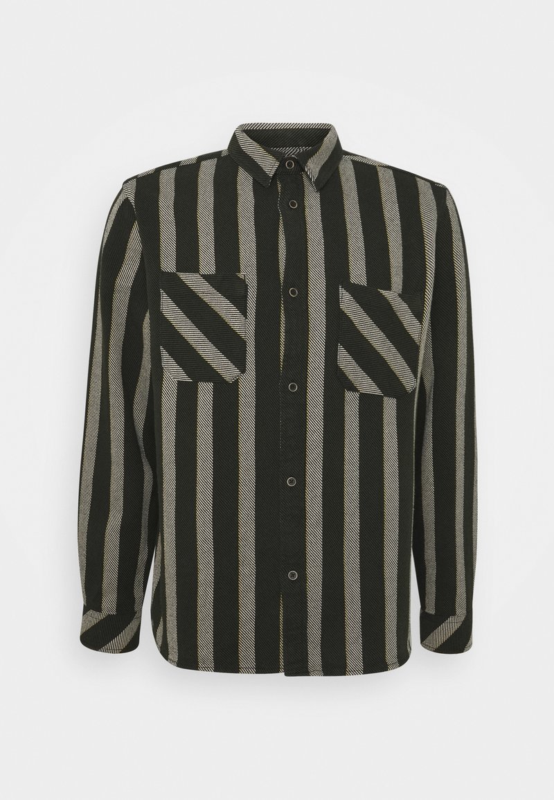Chemise à manches longues boutonnée avec des rayures verticales noires et beiges et deux poches poitrine à rayures diagonales, sur un fond uni clair.