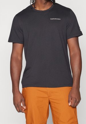 Homme portant un t-shirt noir à manches courtes Peak Performance et un short orange, montré des épaules jusqu'à mi-cuisse.