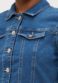 Blå denimjacka med krage, med silverknappar, två bröstfickor och vertikala sömmar. Klassisk design, mellan tvätt.