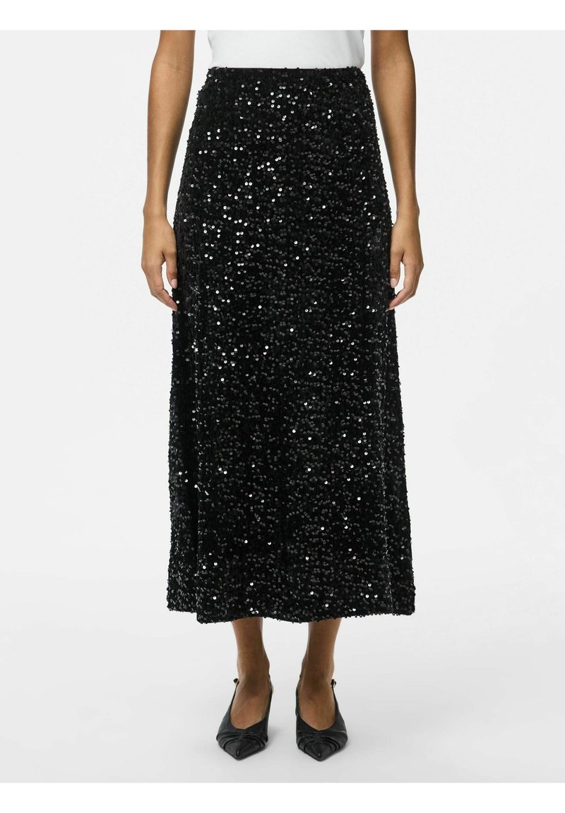 Sorte pailletmaksiskørt med lige design, der har en struktureret overflade og høj talje. Kombineret med spidse sorte sko.