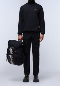 Czarna bluza z okrągłym logo, w zestawie z czarnymi spodniami i dużym czarnym plecakiem z wyrazistymi grafikami i wieloma przegródkami.