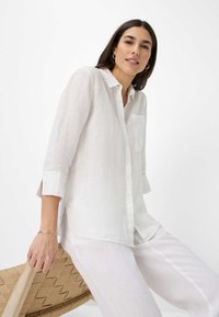 White linen shirt with a button-down collar, chest pocket, and three-quarter sleeves. Smooth texture, relaxed fit, casual style.