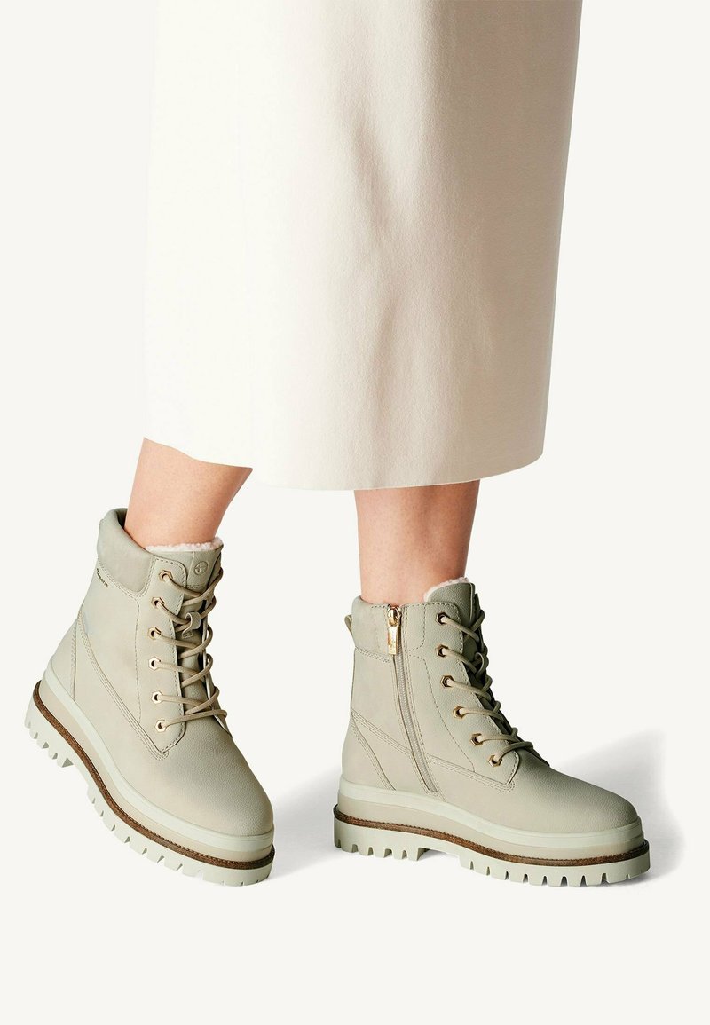Bottes chevilles vert clair en cuir texturé, avec un laçage à l'avant, une fermeture éclair sur le côté et une semelle épaisse et robuste avec un léger talon.