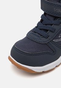 Navy blue athletic shoe with fabric and synthetic upper, textured surface, white midsole, and brown rubber outsole. Features laces and a strap.
