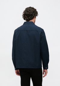 Tummansininen laivastotakki, jossa on kaulus ja napilliset hihansuut, yksivärinen pinta ja suora leikkaus, esitetty takaa.