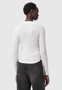Witte lange mouwen top met een textuur van golvende patronen. Ronde halslijn, aansluitend ontwerp, gecombineerd met donkergrijze jeans. Minimalistische stijl, eenvoudige accenten.