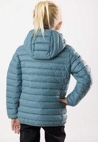 Ljusblå vadderad jacka med huva, med horisontell quiltad sömnad och en slät yta. Inkluderar en liten logotags vid fållen.