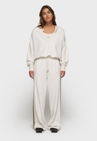 Witte oversized sweatshirt met een V-hals, gecombineerd met bijpassende wijde sweatpants met zijkanten in een contrasterende kleur. Gladde textuur, casual pasvorm.