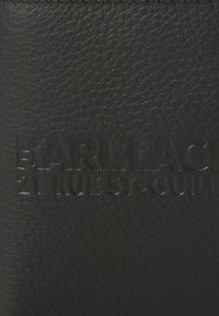 Produs din piele neagră cu o suprafață texturată, având litere debitate, inclusiv "KARL LAGERFELD" și "21 RUE ST. GUILLAUME."