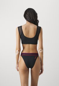 Crni bikini set s uskim gornjim dijelom s mrežastim trakama i donjim dijelom niskog struka s pojasom u ružičastoj boji. Glatka tekstura i minimalistički dizajn.