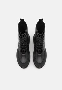 Černé vysoké boty z lesklé kůže s kulatou špičkou, šněrováním vpředu a gumovou podrážkou se strukturovanými detaily.