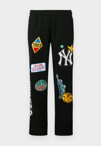 Czarne spodnie dresowe z różnorodnymi kolorowymi naszywkami, w tym logo New York Yankees, grafikami baseballowymi oraz Statuą Wolności.