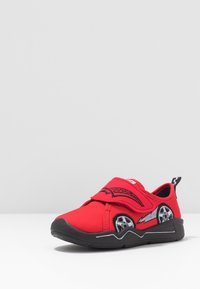 Rode kinderschoen met een zachte stoffen bovenkant, elastische band en zwarte rubberen zool. Heeft autowielafbeeldingen aan de zijkant.