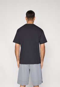 Czarna bawełniana koszulka z krótkim rękawem i okrągłym dekoltem, widoczna od tyłu. Dobraną do niej szare sportowe szorty.