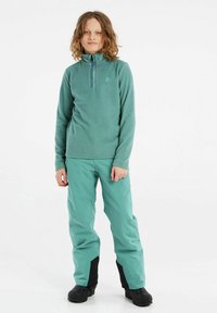 Fleece pullover i blød teal med halv lynlås krave; parret med letvægts teal bukser med sorte accenter; båret med robuste sorte støvler.