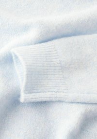 Pull en cachemire bleu clair avec un poignet côtelé texturé et un tissu doux et lisse. La surface présente un motif subtil et délicat.