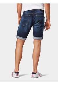 Tummat farkkushortsit, joissa on käärityt lahkeet, kaksi takataskua ja sileä pinta, yhdistettynä valkoisiin tennareihin, joissa on punaisia ja laivastonsinisiä yksityiskohtia.